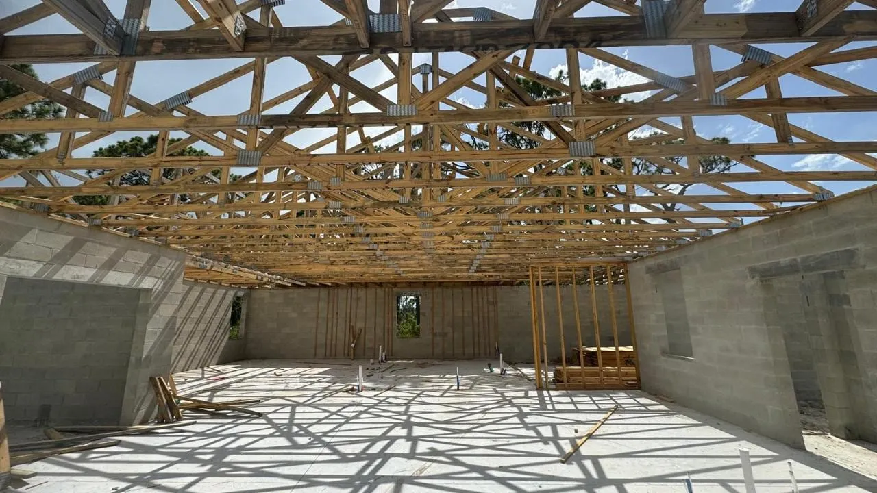 Interior en obra con el entramado de cerchas de madera proyectando sombras sobre la losa