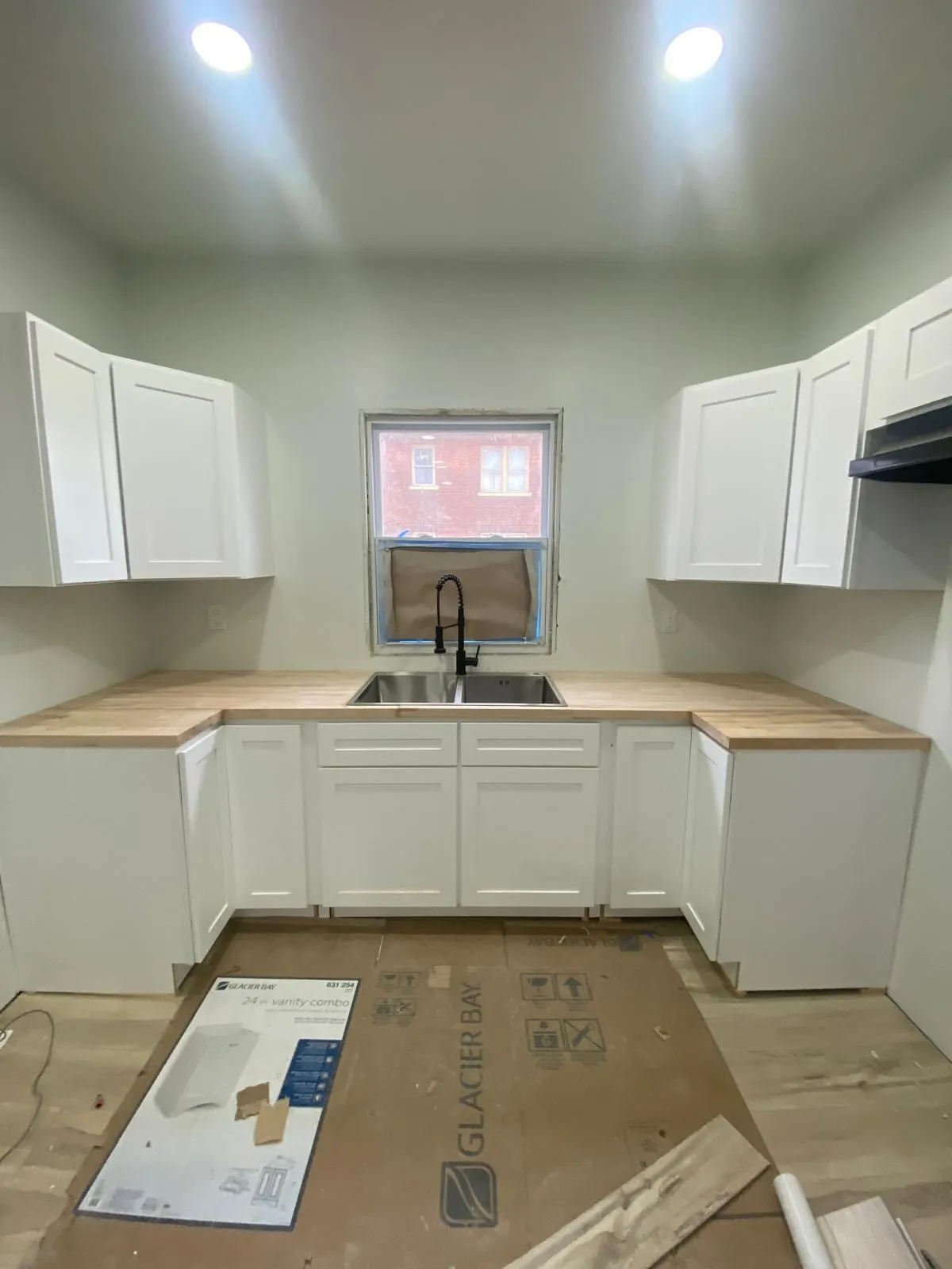 Cocina terminada con gabinetes blancos, mesón de madera y grifo negro